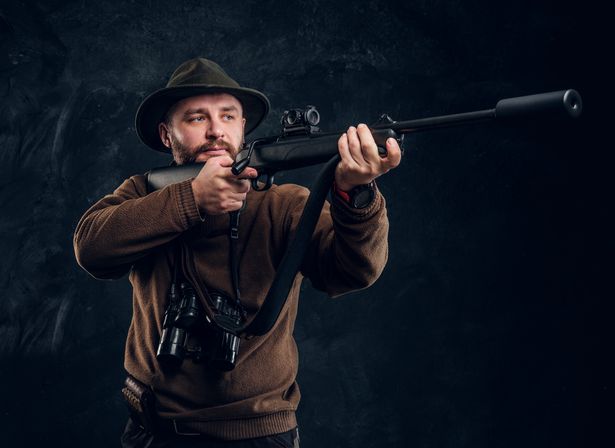 Portrait of a bearded hunter holding a rifle. Studio photo against dark wall background